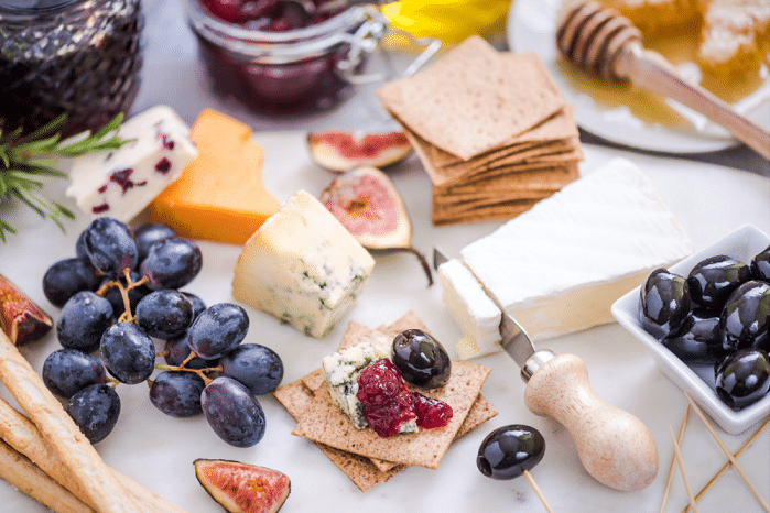 cheese board with wide selection of appetizers including grapes, jams, & fig