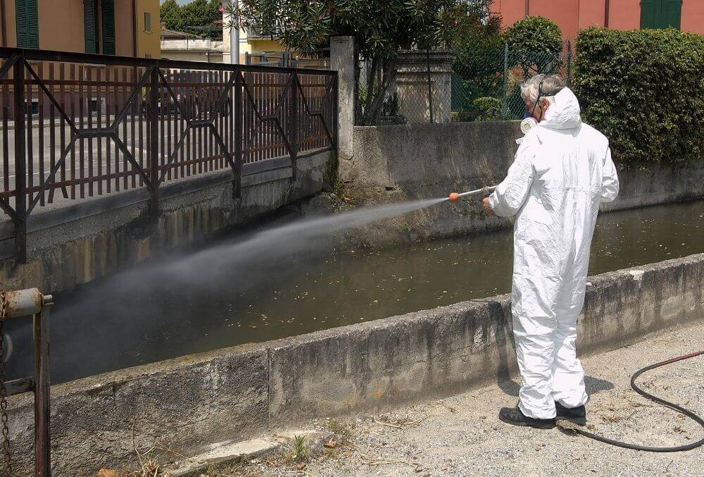 Man in white suit disinfecting sidewalk of metropolitan area